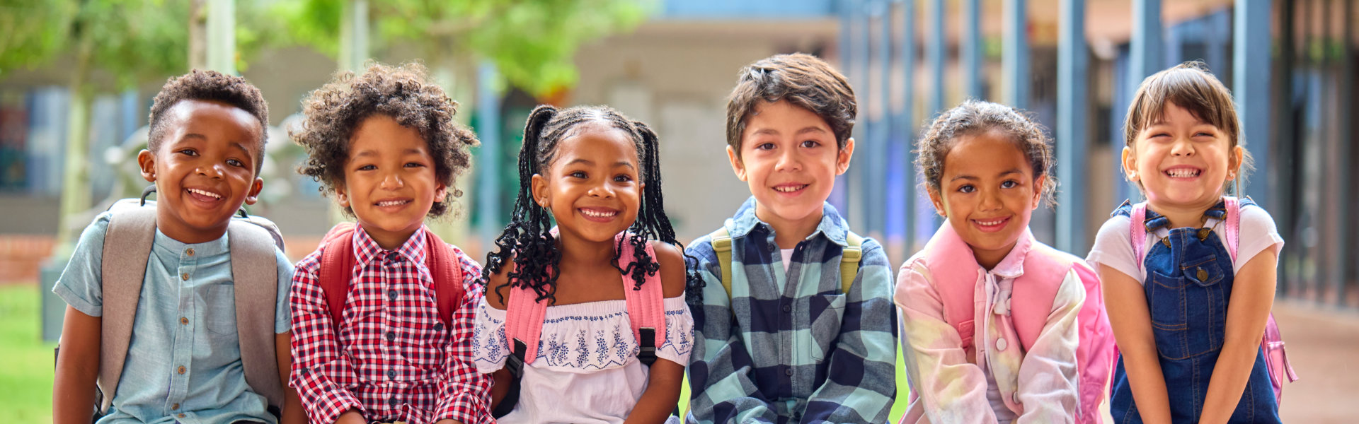 Portrait Of Multi-Cultural Elementary School Pupils Sitting On Wall Outdoors At School